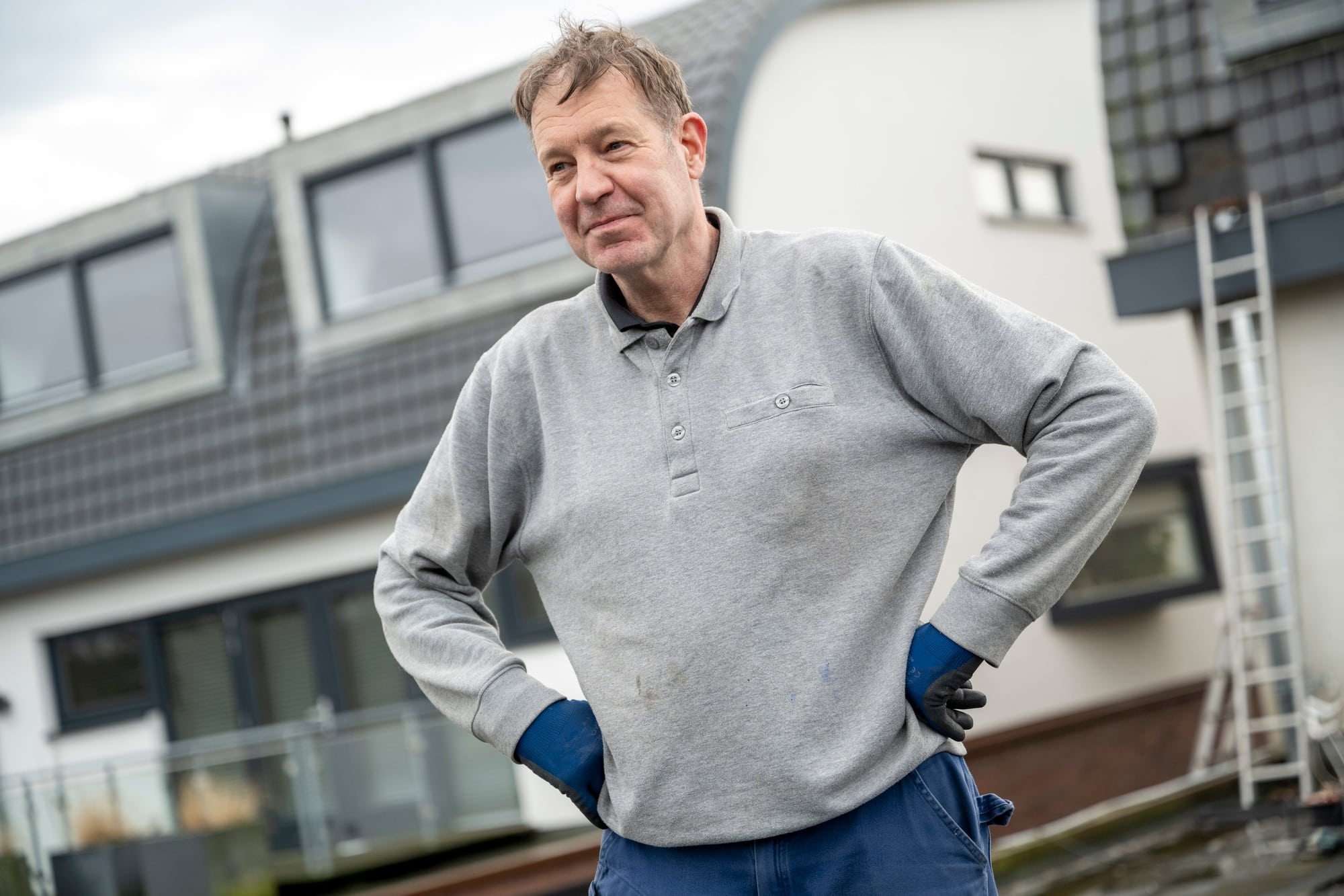 Confident man standing with hands on hips outside a modern home.